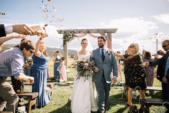 Couple walking down the aisle after getting married, guests are throwing confetti