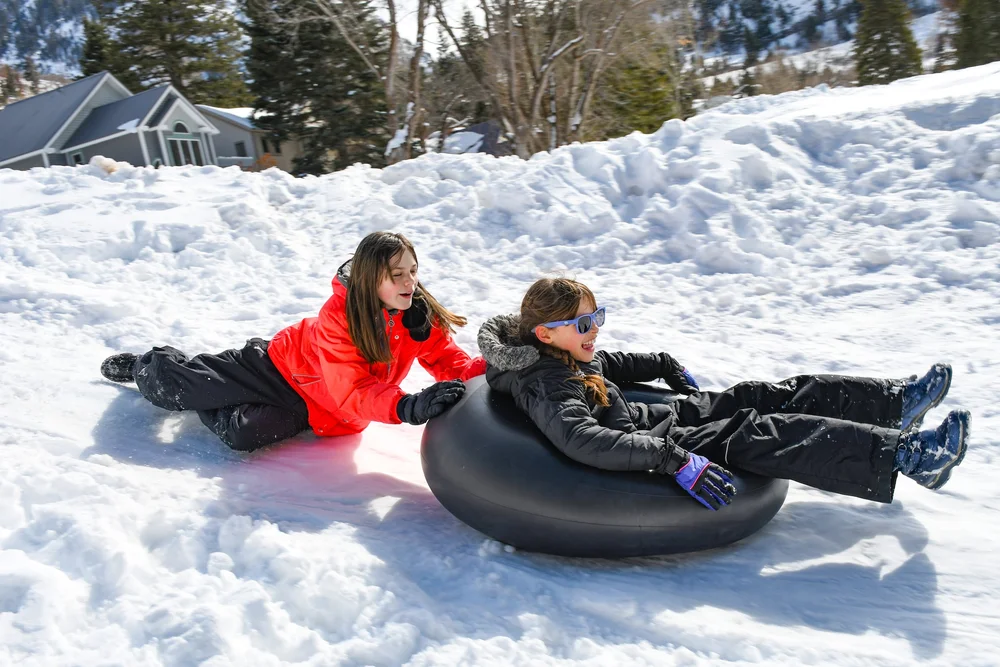kid on a snow tube being pushed by another kid