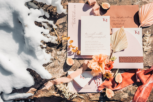 Pink wedding invitation surrounded by snow, leaves, and ribbons