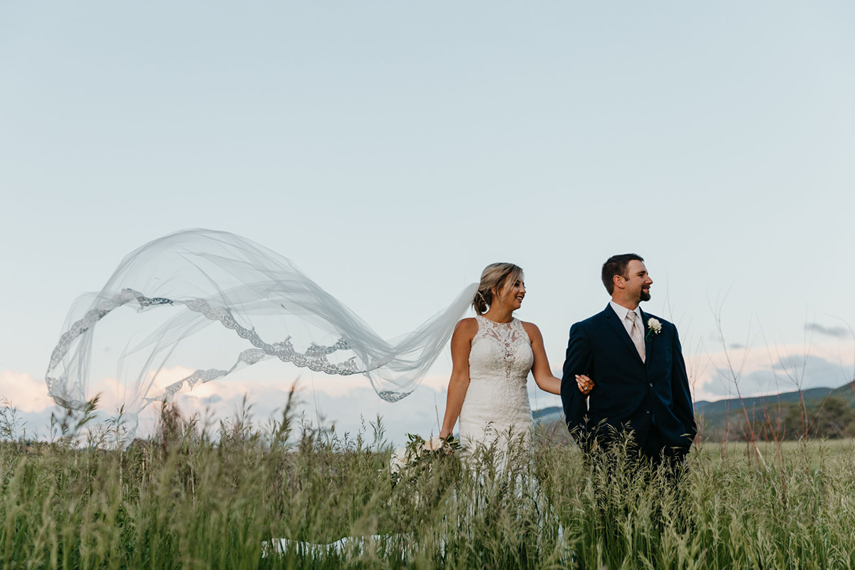 Bride and groom standing in a field with the wind blowing the bride's veil
