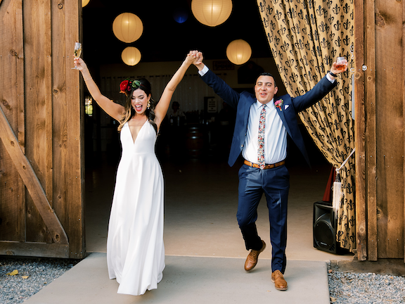 Couple walking out of barn celebrating with champagne and arms in the air