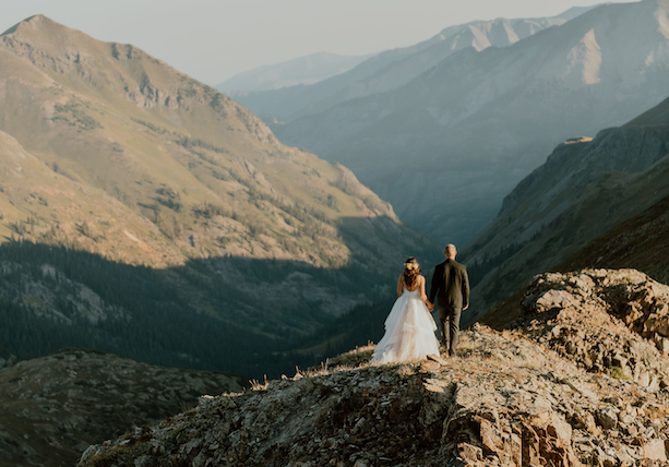 bride and groom standing on the top of a mountain looking into the distance