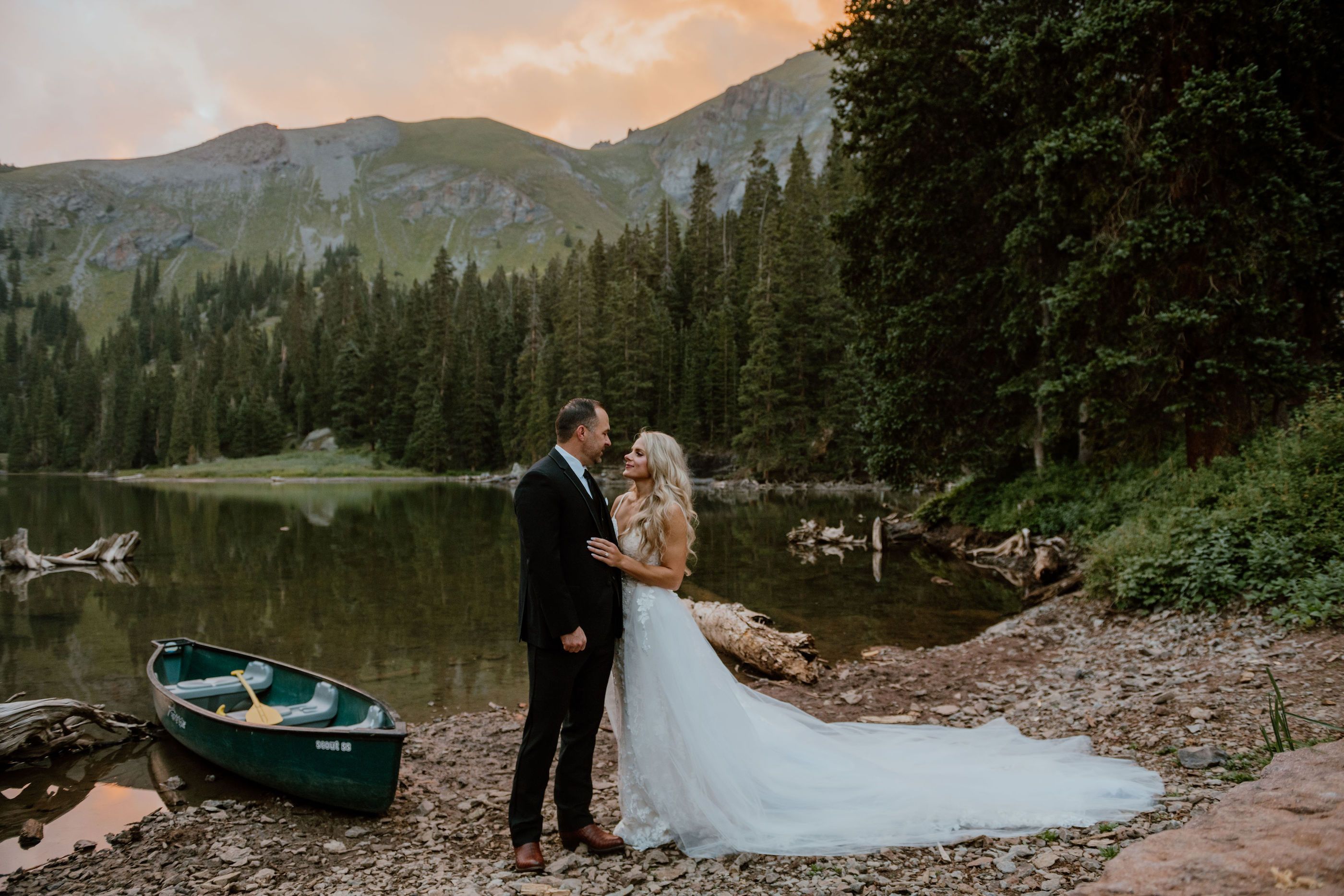 bride and groom embracing near a lake with a canoe
